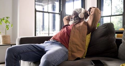 Senior man relaxing on couch with headphones in cozy living room