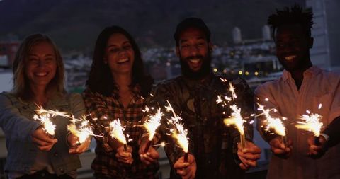 Joyful friends celebrating with sparklers on rooftop at night