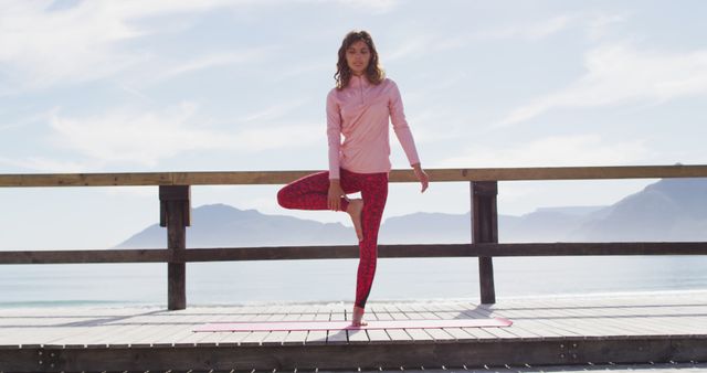 Woman practicing tree pose on seaside boardwalk in serene morning light, ideal for promoting wellness, fitness routines, yoga classes, mindfulness, and outdoor activities on websites or social media.