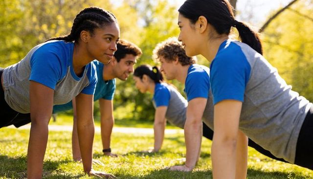 Holding plank together in park, diverse adults training outdoors, team fitness