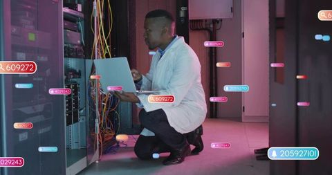Kneeling it technician inspecting server rack with laptop and network cabling in magenta