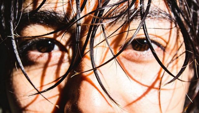 Intense closeup asian adult brown eyes wet hair strands casting dramatic studio shadows