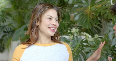 Woman smiling and chatting with friend amid lush monstera foliage in conservatory
