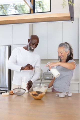 Senior couple making batter together in bright modern kitchen, baking at island counter