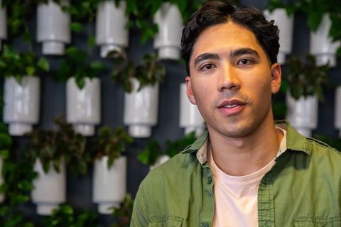 Young man posing in coworking cafe with vertical plant wall, modern biophilic headshot