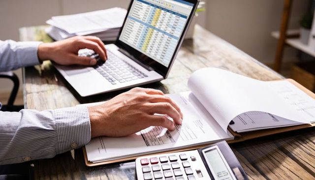 Hands reviewing financial forms and excel spreadsheet on laptop while calculating expenses