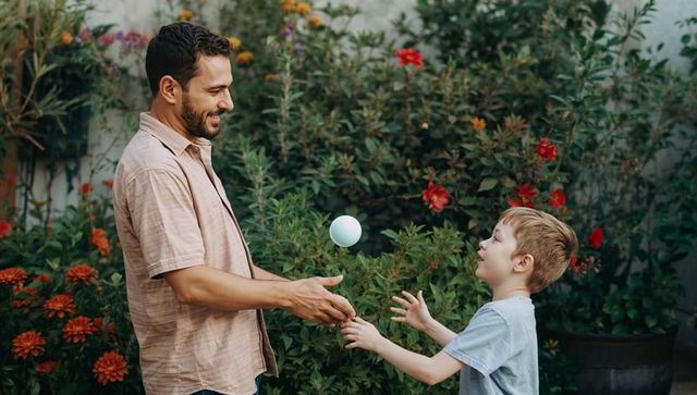 Father and son playing catch in flower garden tossing ball and laughing outdoors