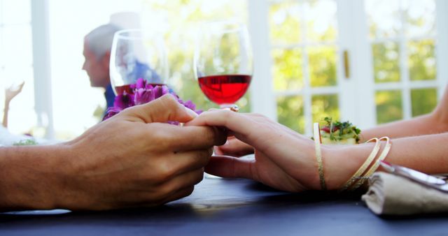 A man and woman engage in a romantic gesture, holding hands across a table with wine glasses and a meal in the background, with copy space. Capturing a moment of intimacy, the image conveys a sense of connection and celebration, in a fine dining setting.