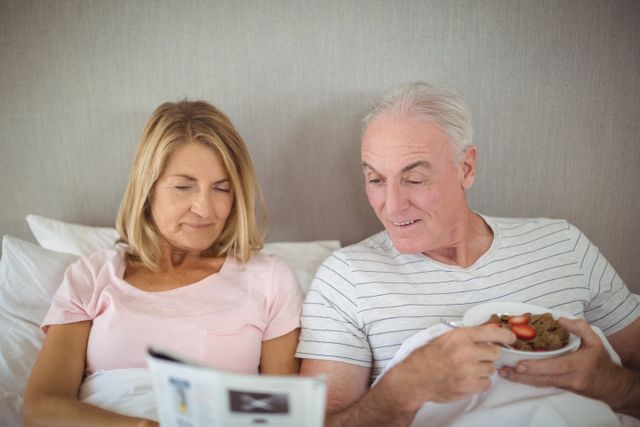 Older couple enjoying a peaceful morning together, reading the newspaper and having breakfast in bed. Perfect for illustrating themes of retirement, love, and relaxed lifestyle. Suitable for use in advertisements, health and wellness blogs, retirement planning brochures, and lifestyle magazines.