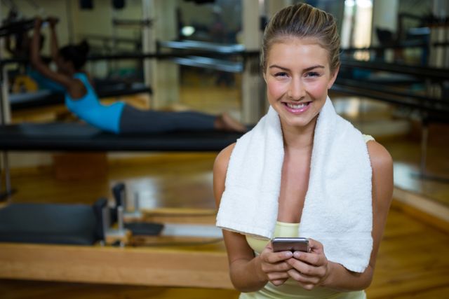 Fit woman smiling and using mobile phone after workout in gym. Perfect for promoting fitness apps, gym memberships, healthy lifestyle blogs, and exercise equipment. Highlights the integration of technology in fitness routines.