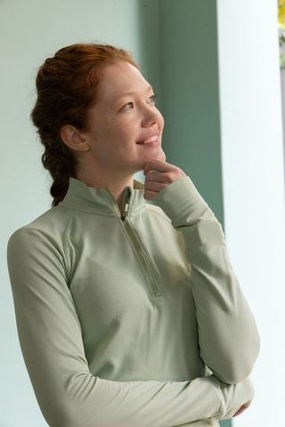 Serene woman gazing upward in sage quarter-zip pullover, braided hair, soft daylight