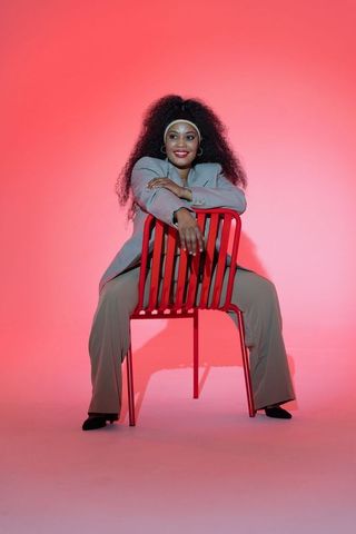 Confident african american woman sitting backward on red chair wearing blazer and headband