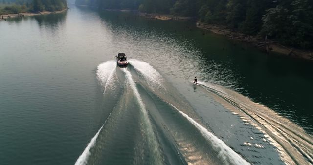 A motorboat creates a wake on a serene lake as it tows a water skier, with copy space - Download Free Stock Photos Pikwizard.com