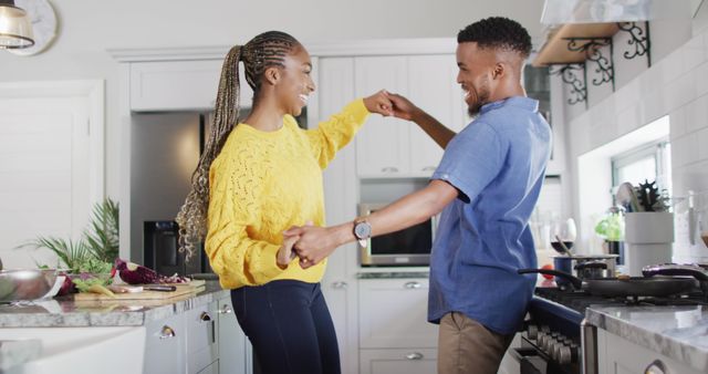 Happy couple engaging in a playful dance while preparing a meal in a brightly lit, modern kitchen. Both are smiling and enjoying the moment. Useful for content related to love, relationships, home activities, cooking, and lifestyle inspiration.