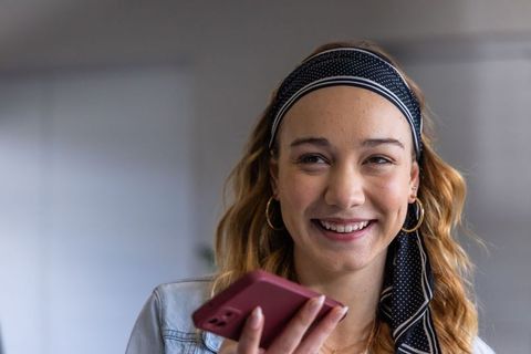 Smiling young woman speaking into pink smartphone, denim jacket, headband, casual portrait