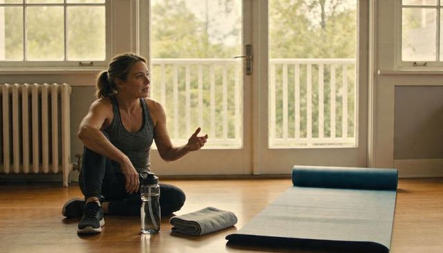 Woman talking after home workout near sunlit french doors yoga mat water bottle