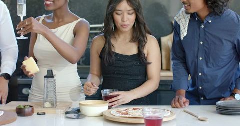 Diverse friends preparing pizza and toasting with champagne in stylish home kitchen