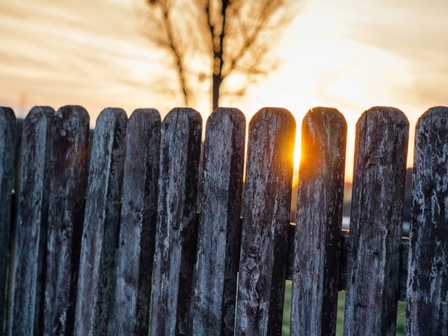 Weathered wooden fence standing against a warm, golden sunset with a softly focused tree in the background. Ideal for conveying themes of rural serenity, peaceful landscapes, and natural beauty. Perfect for use in blogs, nature-inspired web content, wallpapers, and prints celebrating countryside life.