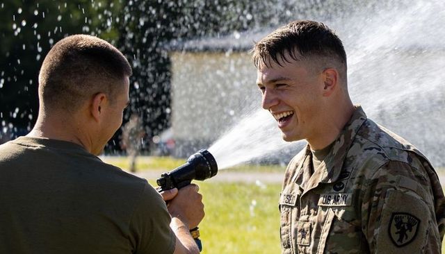 Soldier laughing while comrade spraying water with hose during military training