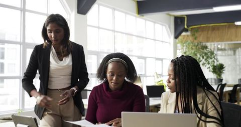 Multiracial professional women collaborating at desk in bright modern office