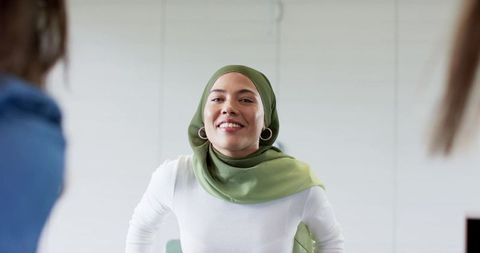 Confident businesswoman smiling presenting in meeting room wearing olive hijab