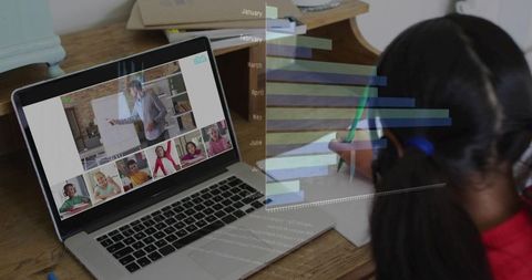 Schoolgirl writing while learning in virtual classroom at home desk with laptop and chart overlay