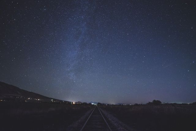 Milky Way galaxy magnificently spread across starry night sky above solitary railroad track in wilderness. Perfect for backgrounds, travel blogs, nature and astronomy articles, and posters conveying themes of solitude, exploration, and the vastness of the universe.