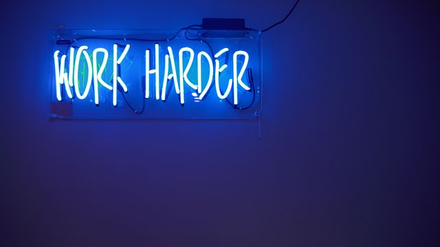Blue neon sign with 'Work Harder' message glowing in a dark room. Perfect for use in inspirational and motivational designs, office decors, promotional materials, and social media posts to encourage productivity and positive thinking.