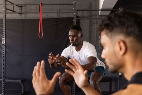 Black man and training partner performing partner squats in urban gym with squat rack