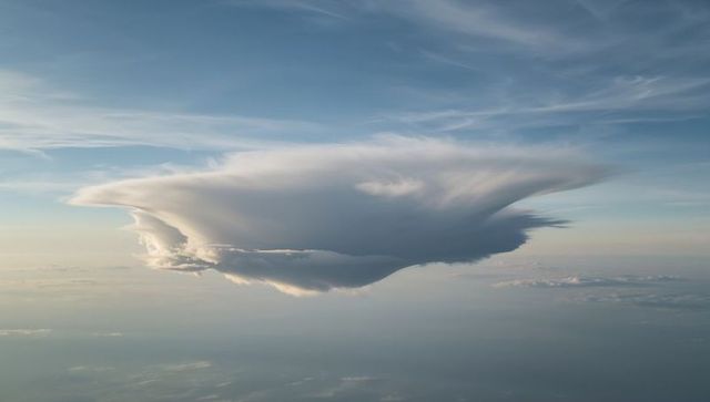 Hovering anvil cloud above calm horizon with sunlit edges and layered cirrus streaks