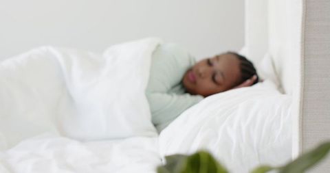 African american woman resting on white bed in minimalist bedroom, serene morning calm