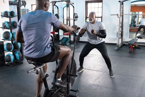 African american trainer coaching client on air bike in modern gym