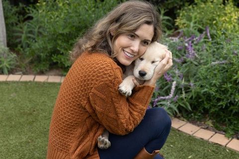 Woman cuddling golden retriever puppy in garden wearing rust cable knit sweater