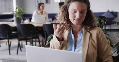Businesswoman Communicating via Smartphone and Laptop in Office