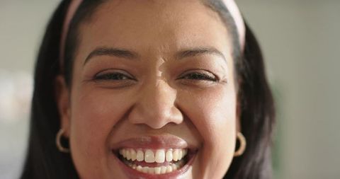 African american woman smiling with bright teeth wearing pink headband and gold hoop earrings