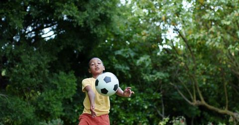 African american boy reaching for soccer ball in lush green park, active outdoor play