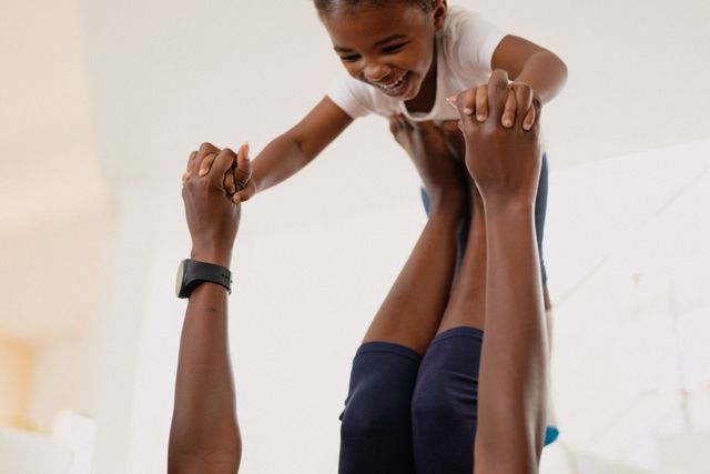 This image captures a joyful moment between an African American mother and her daughter playing and exercising together at home. It is perfect for use in articles or advertisements about family bonding, parenting, home activities, and promoting a healthy lifestyle. The image conveys themes of love, happiness, and togetherness.