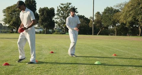Diverse Male Cricket Players Running Cone Drill on Field in White Kits and Black Caps