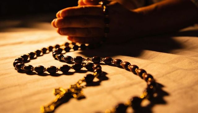 Hands clasping rosary beads with gold crucifix under warm light for prayer and devotion