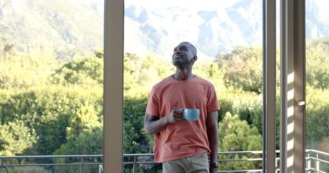 African American man standing on balcony holding mug gazing at mountain view