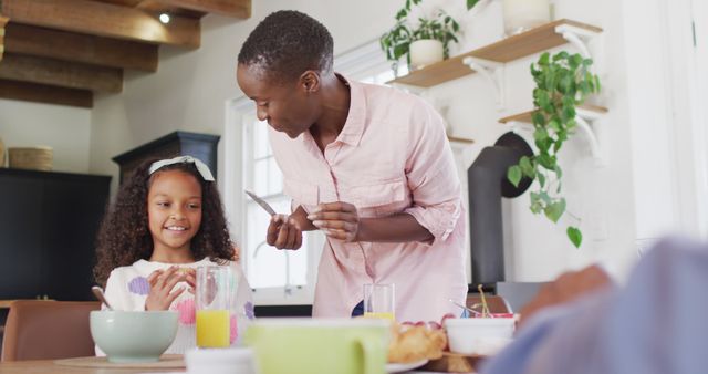 Image of happy african american mother buttering bread for daughter at family breakfast table. Family, domestic life and togetherness concept digitally generated image.