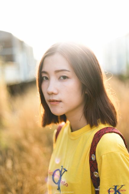 Young woman standing outdoors in sunset light, wearing yellow t-shirt and shoulder bag. Could be used for lifestyle blogs, fashion photography, advertising, youth campaigns, or promoting casual wear.