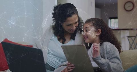Mother and daughter sharing tablet on couch with laptop, home learning and global network