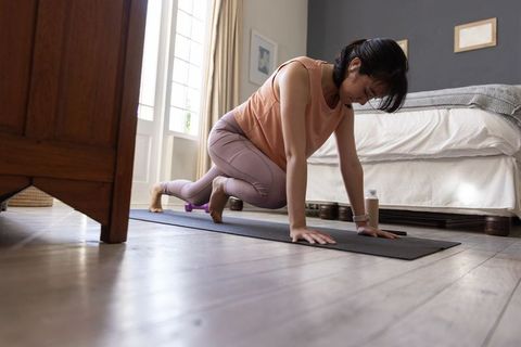 Asian woman performing crawling core exercise on yoga mat in bright bedroom for home fitness