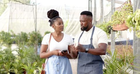 Customer and Employee Discussing Plants in Bright Greenhouse Setting