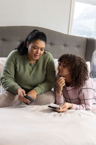 African american mother and teen daughter sharing cozy smartphone moment on bed at home