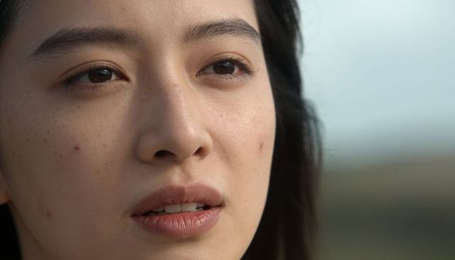 Gazing asian woman showing natural skin texture, freckles and acne in daylight close-up