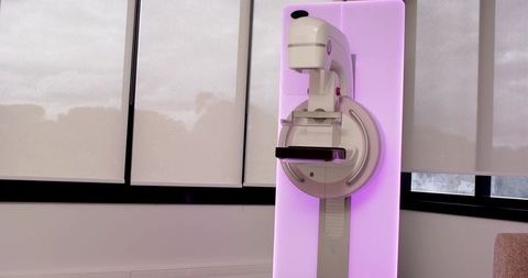 Mammography unit showing compression paddle on pink backlit panel in modern clinic