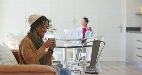 Cozy housemates enjoying coffee, one working on laptop in bright minimalist living room