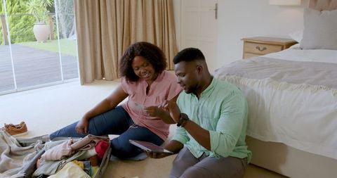 Couple Preparing for Vacation Using Tablet and Packing Suitcase
